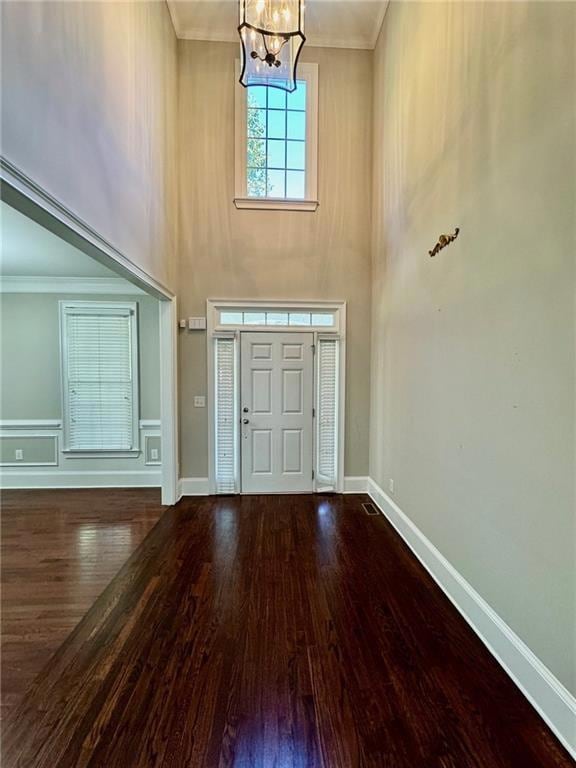 Entrance foyer with crown molding, a high ceiling, dark wood-style flooring, and a chandelier