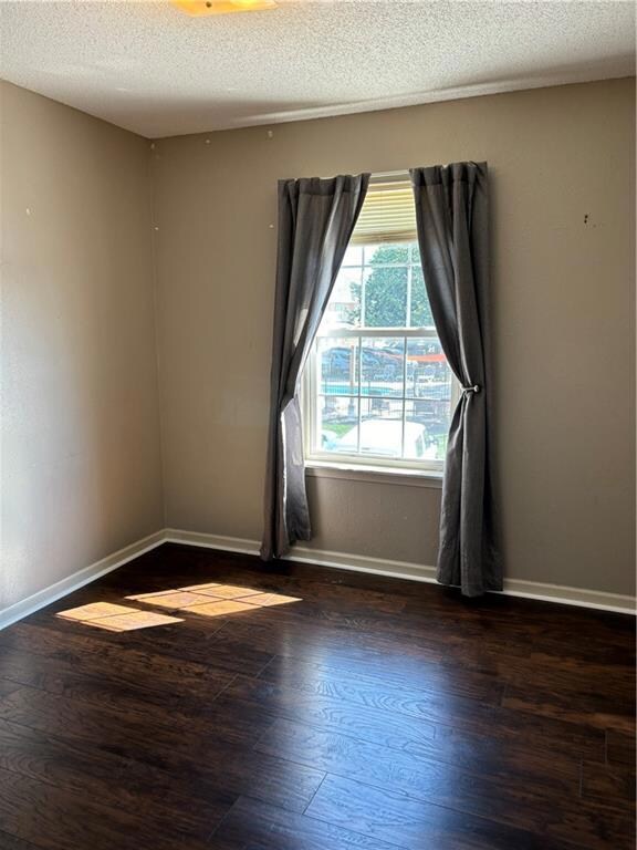 Empty room featuring dark hardwood / wood-style floors and a textured ceiling