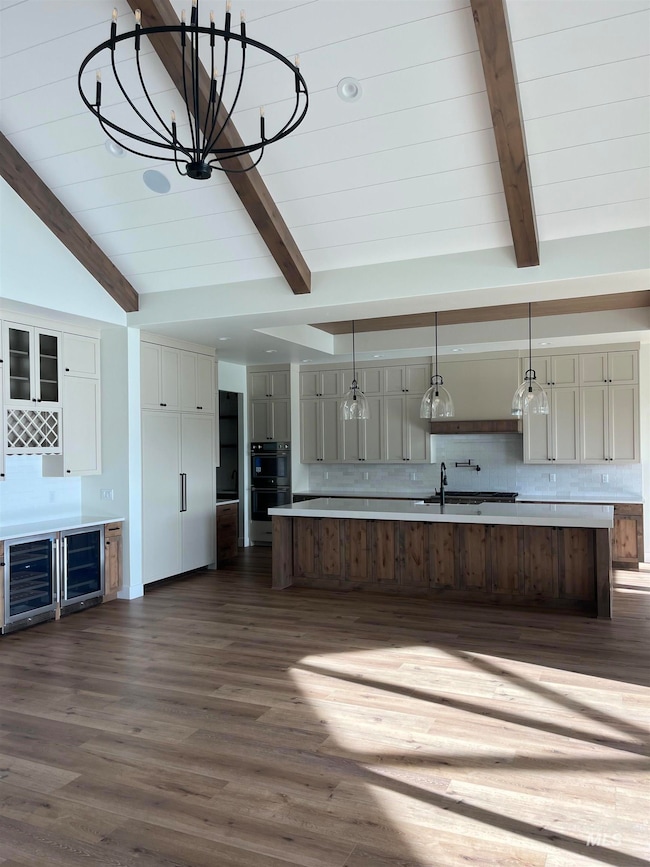 Kitchen with decorative light fixtures, a large island with sink, dark wood-style floors, decorative backsplash, and glass insert cabinets