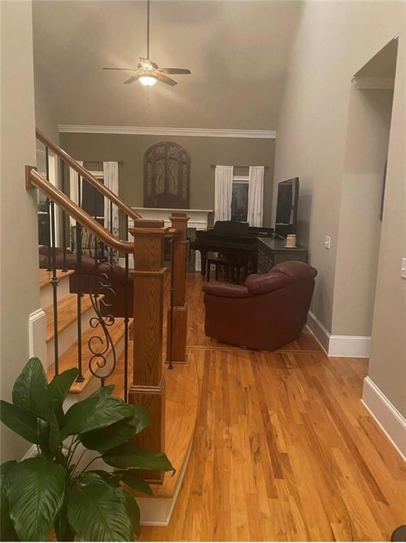 Living area with a ceiling fan, crown molding, wood finished floors, and stairs