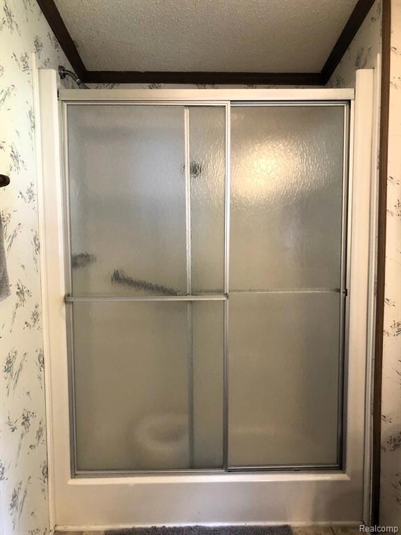 Bathroom featuring a textured ceiling, wallpapered walls, a shower stall, and crown molding