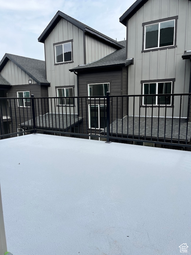 Back of property featuring board and batten siding, roof with shingles, and a balcony