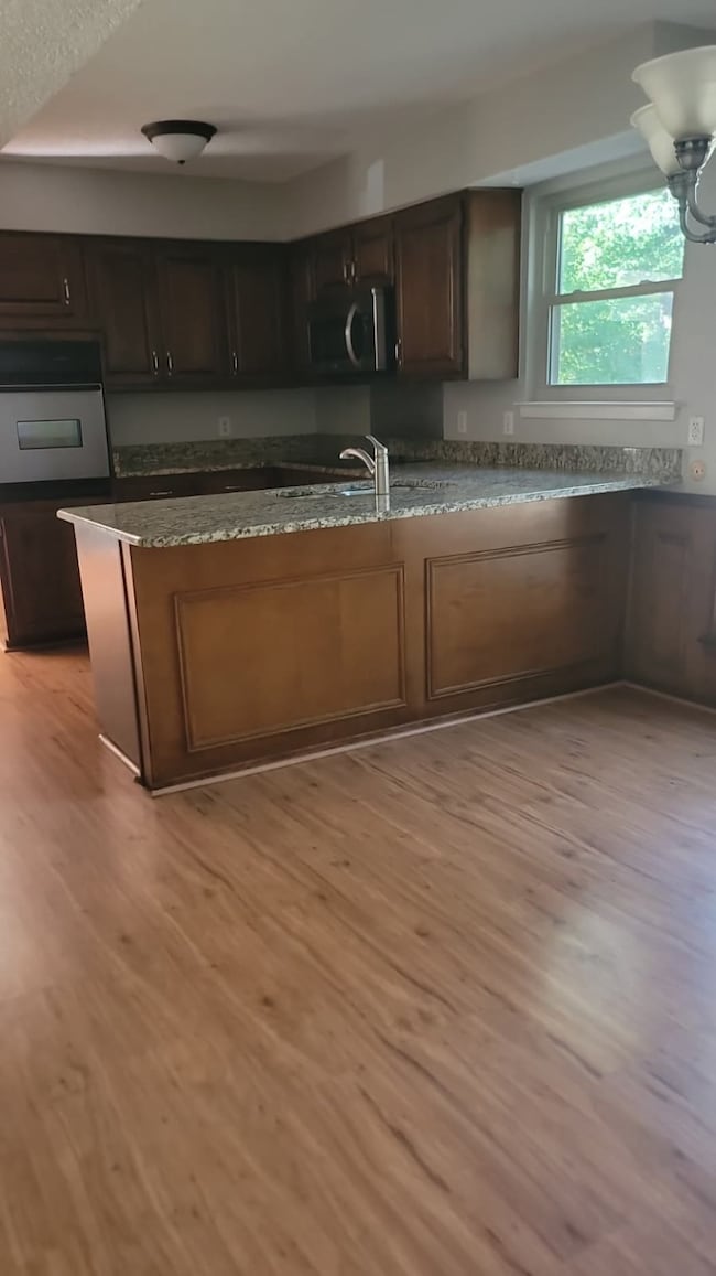 Kitchen featuring stainless steel appliances, dark stone countertops, light wood-type flooring, and dark brown cabinetry