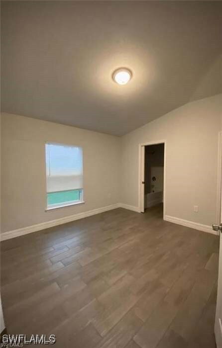 Spare room featuring vaulted ceiling, dark wood-st