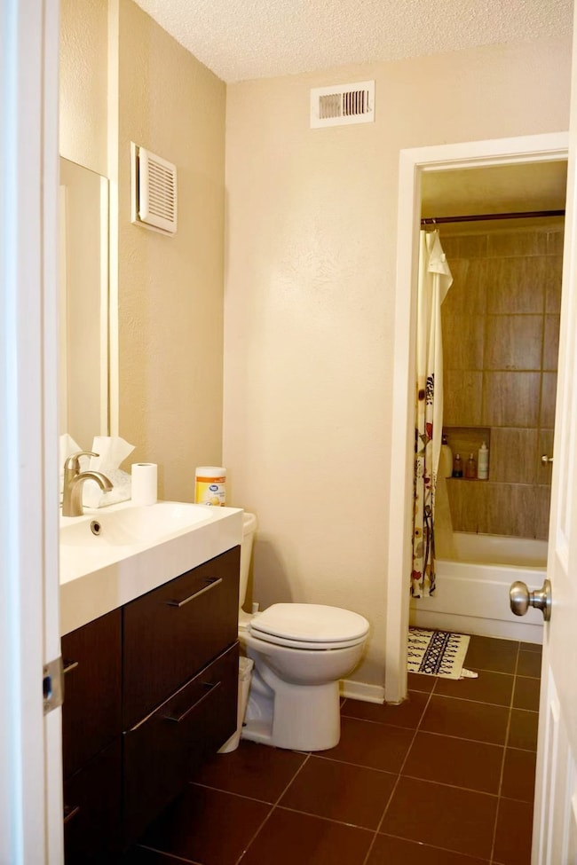 Bathroom with vanity, dark tile patterned floors, shower / bath combination with curtain, and a textured ceiling