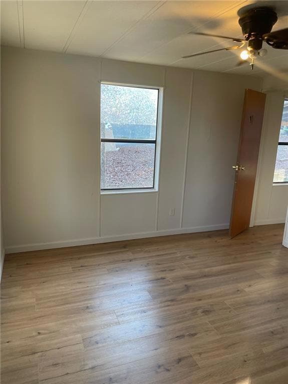 Unfurnished room with healthy amount of natural light, light wood-style floors, a ceiling fan, and a decorative wall