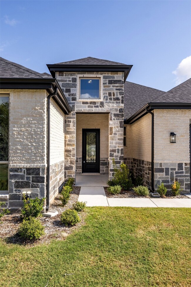 Entrance to property with stone siding, a lawn, brick siding, and a shingled roof