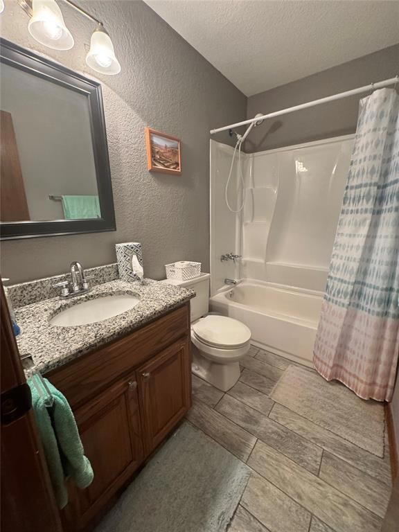 Full bathroom featuring shower / bathtub combination with curtain, a textured wall, vanity, and a textured ceiling