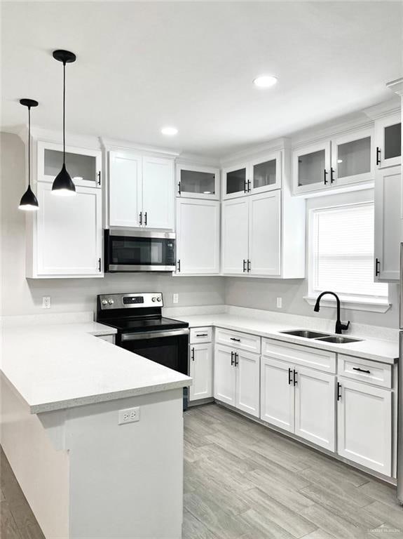 Kitchen with glass insert cabinets, light wood-type flooring, appliances with stainless steel finishes, recessed lighting, and a peninsula