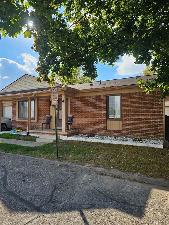 Ranch-style home featuring brick siding, covered porch, a garage, and a front lawn