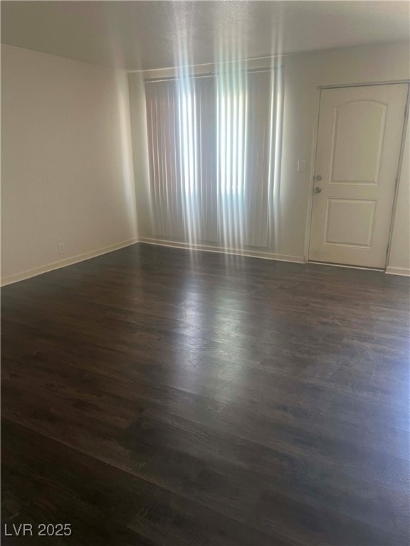 Unfurnished room featuring baseboards and dark woo