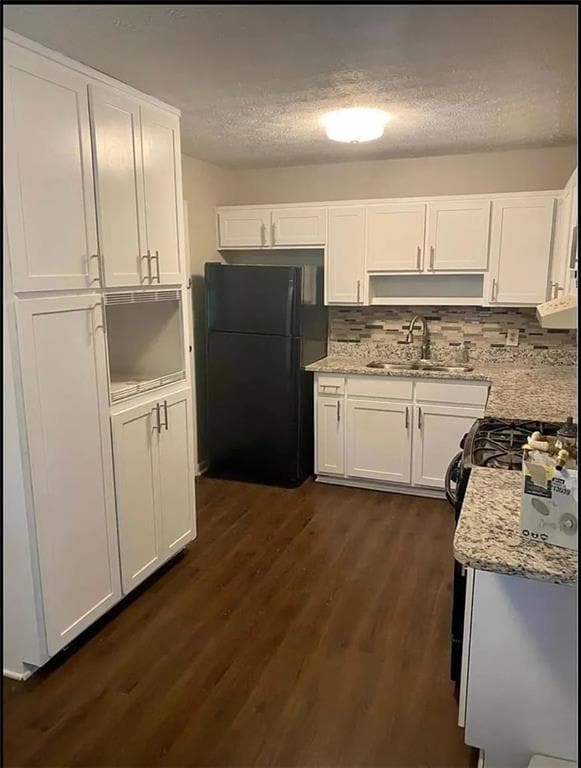Kitchen with freestanding refrigerator, a sink, white cabinetry, dark wood-style floors, and a textured ceiling