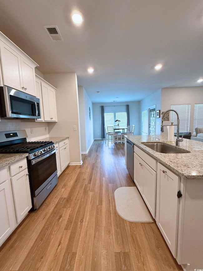 Kitchen with stainless steel appliances, white cabinets, light wood-style flooring, light stone counters, and recessed lighting