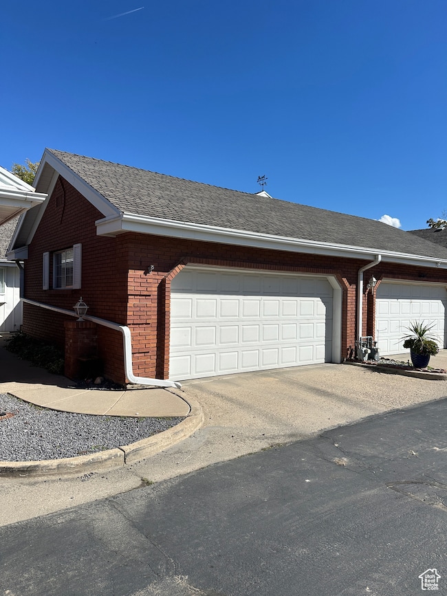 View of side of property with a shingled roof, brick siding, driveway, and a garage