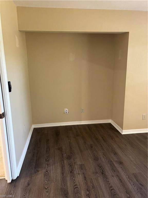 Spare room featuring dark wood-style flooring and baseboards