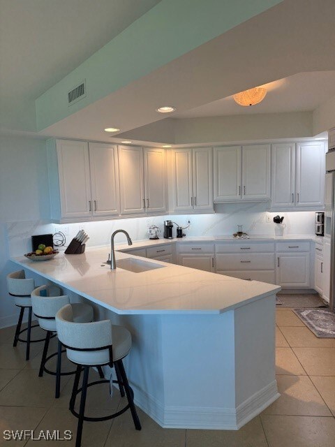 Kitchen featuring white cabinets, light tile patterned floors, a peninsula, a breakfast bar area, and recessed lighting