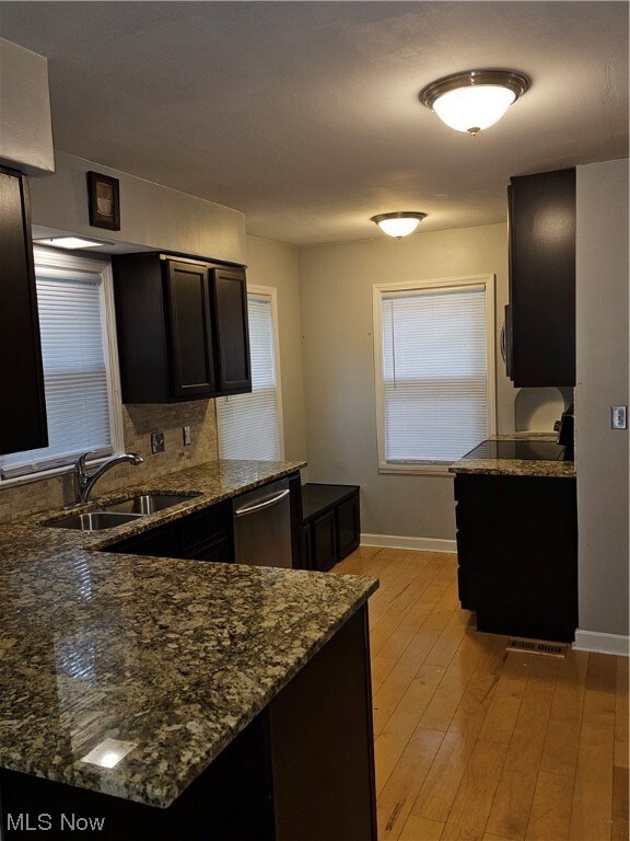 Kitchen with tasteful backsplash, light hardwood floors, sink, dark stone countertops, and dishwashing machine