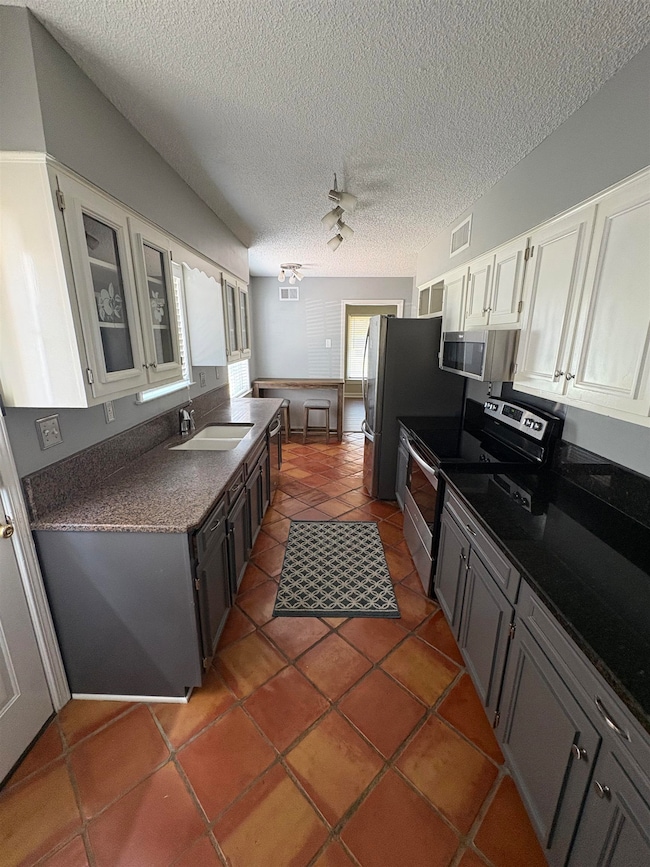 Kitchen with stainless steel appliances, dark countertops, glass insert cabinets, tile patterned floors, and a textured ceiling