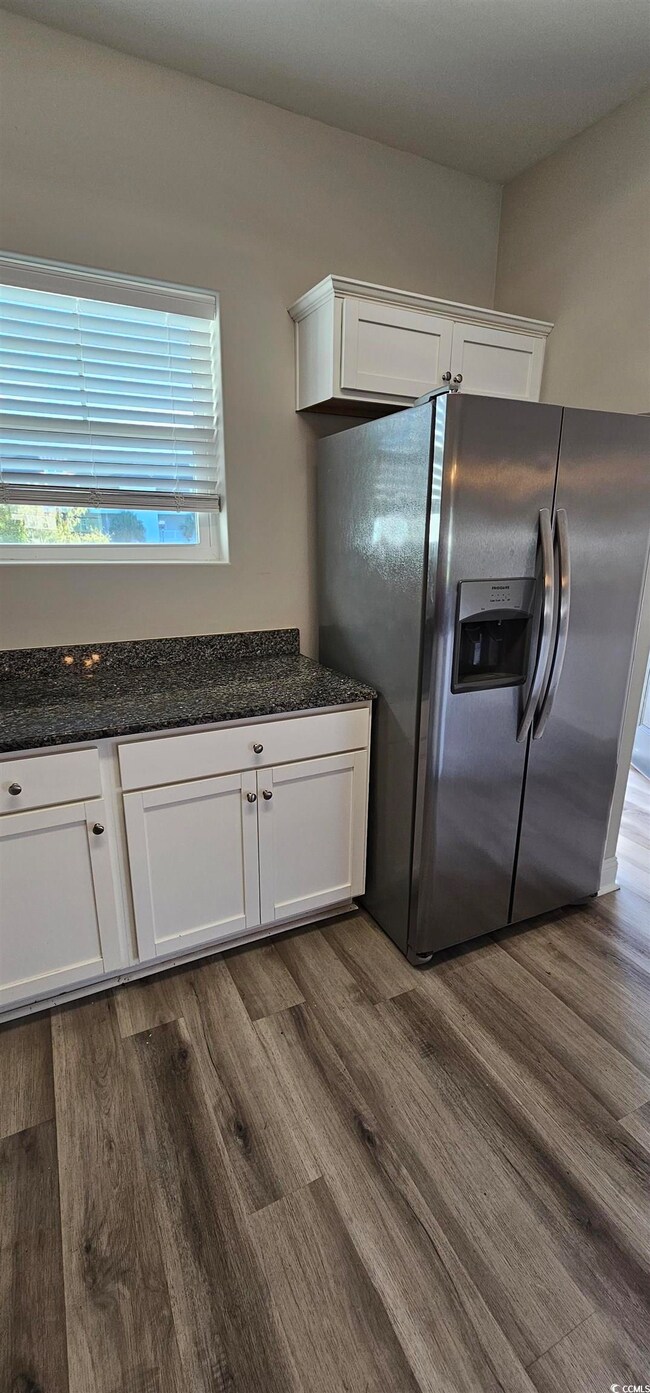 Kitchen with stainless steel fridge with ice dispenser, dark wood-type flooring, white cabinets, and dark stone counters