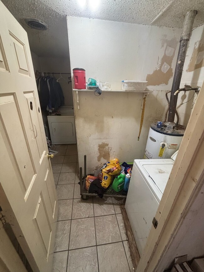 Washroom with light tile patterned floors, a textured ceiling, water heater, and washer / dryer