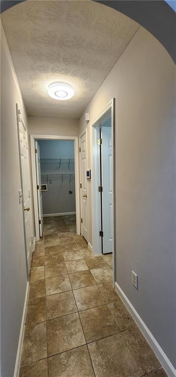 Hall featuring arched walkways, baseboards, and a textured ceiling