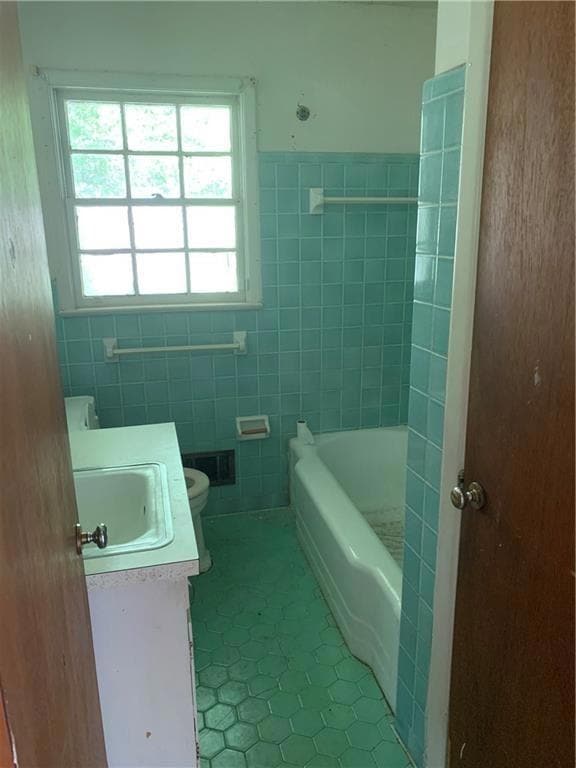 Full bathroom featuring tile patterned flooring, plenty of natural light, tile walls, toilet, and a tub