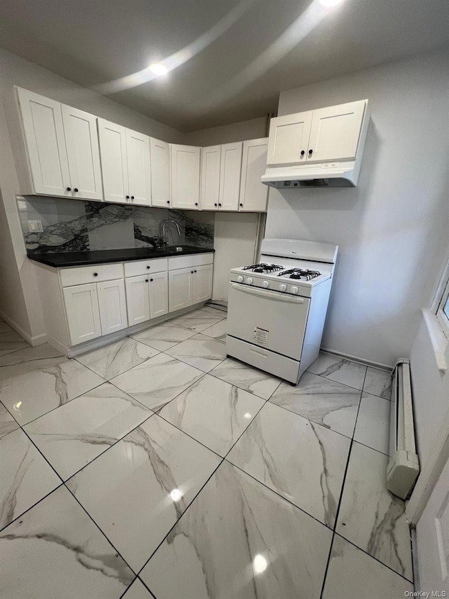 Kitchen with gas range gas stove, white cabinetry, light marble finish floors, dark countertops, and under cabinet range hood