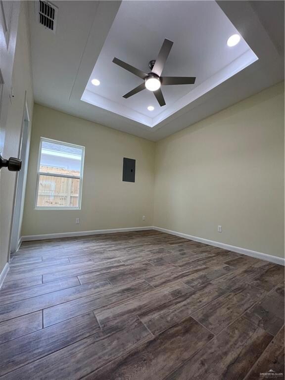 Empty room with dark wood-type flooring, ceiling fan, and a tray ceiling