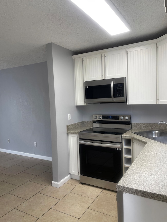 Kitchen featuring stainless steel appliances, a textured ceiling, white cabinetry, and light tile patterned floors