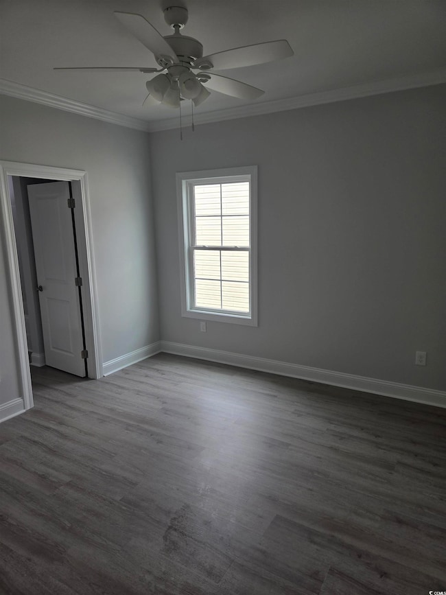 Empty room with dark wood-type flooring, baseboards, a ceiling fan, and ornamental molding