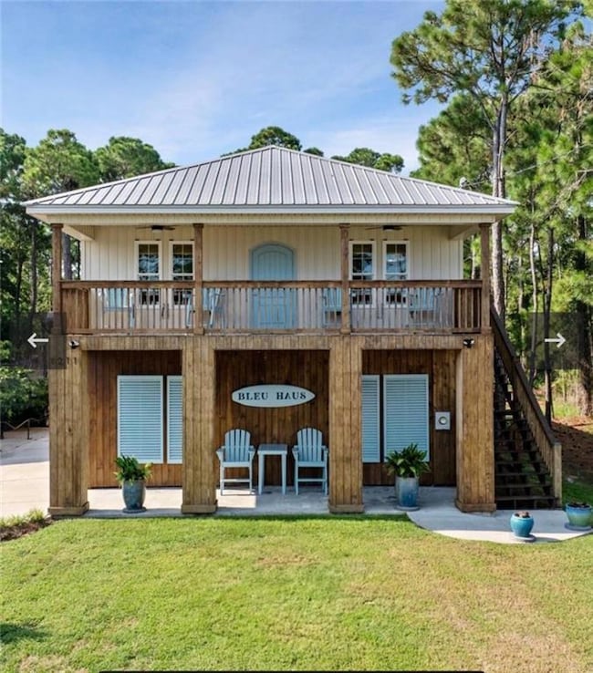 Back of property featuring stairs, a balcony, a lawn, and a metal roof