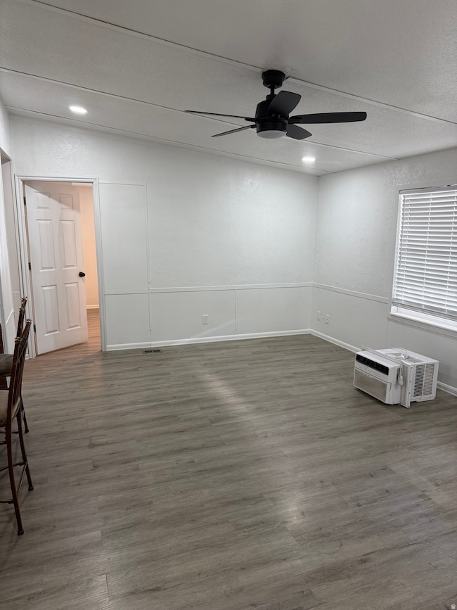Unfurnished room with dark wood-style flooring, ceiling fan, and a wall mounted air conditioner