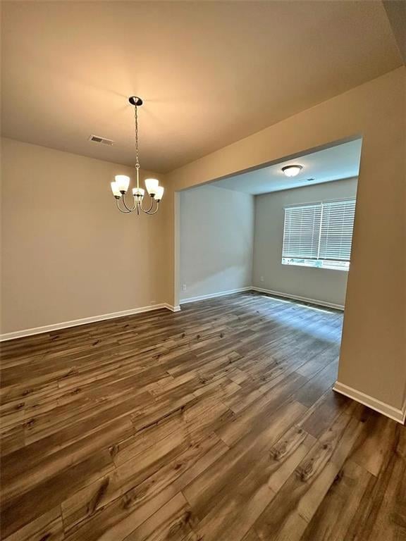 Spare room with dark wood finished floors and a chandelier