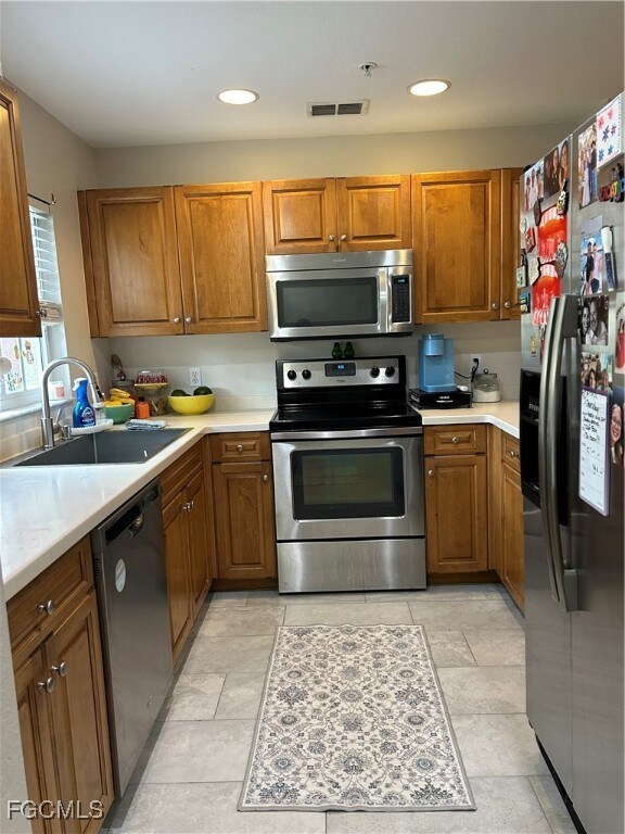 Kitchen featuring stainless appliances, brown cabinets, Corian countertops, and recessed lighting.