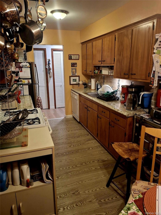 Kitchen featuring dark wood-style floors, white appliances, brown cabinets, and light stone counters