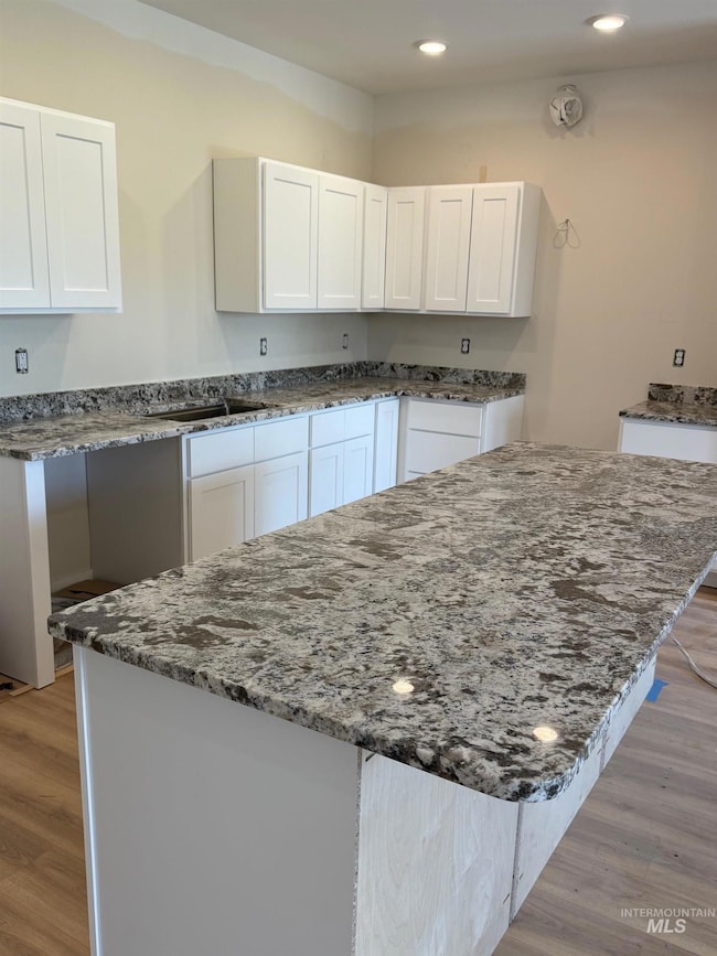 Kitchen with dark stone countertops, white cabinets, light wood finished floors, a center island, and recessed lighting