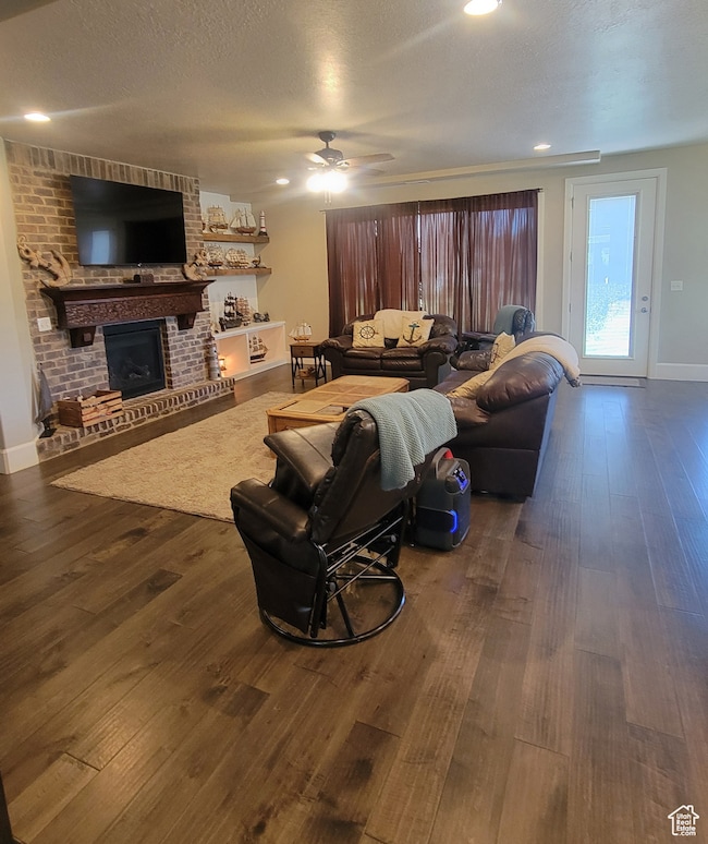 Living area with a textured ceiling, dark wood finished floors, a fireplace, recessed lighting, and a ceiling fan