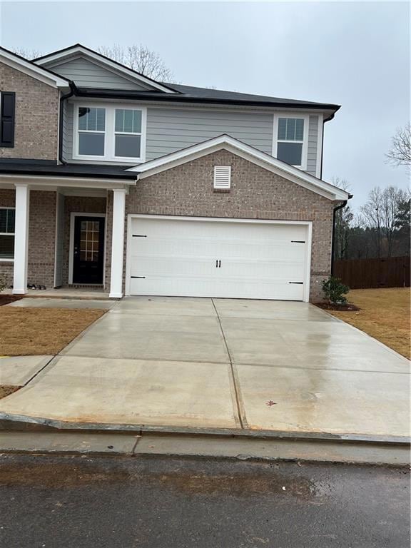 View of front facade with brick siding, a garage, driveway, and covered porch