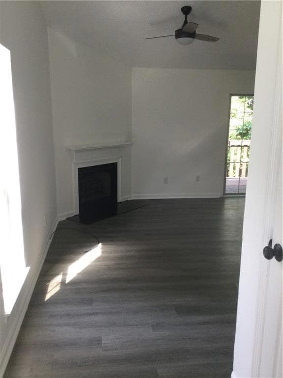 Unfurnished living room with a ceiling fan, a fireplace, and dark wood-style floors