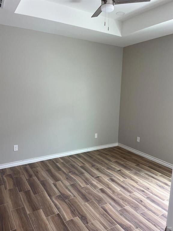 Unfurnished room featuring a ceiling fan, dark wood-style floors, and baseboards