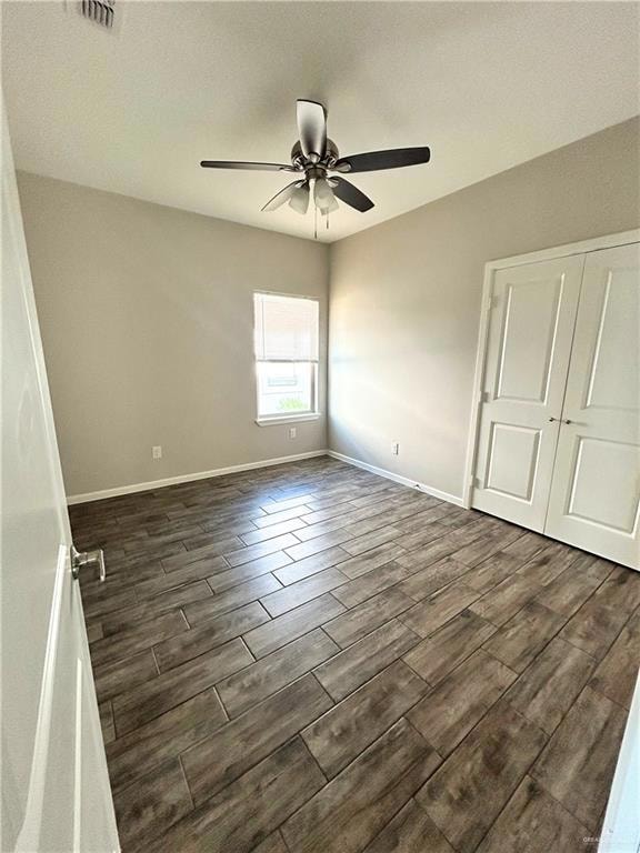 Unfurnished bedroom with a ceiling fan, visible vents, dark wood finished floors, baseboards, and a closet