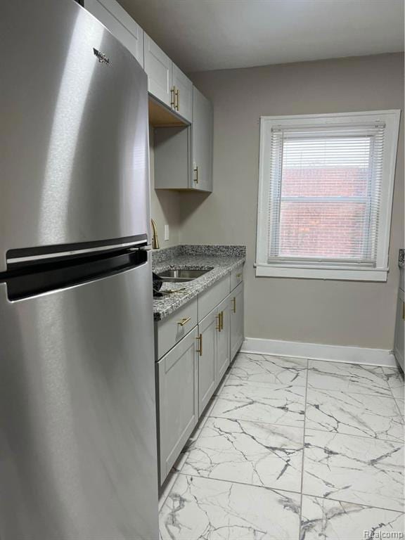 Kitchen featuring freestanding refrigerator, light marble finish floors, gray cabinets, and dark stone counters