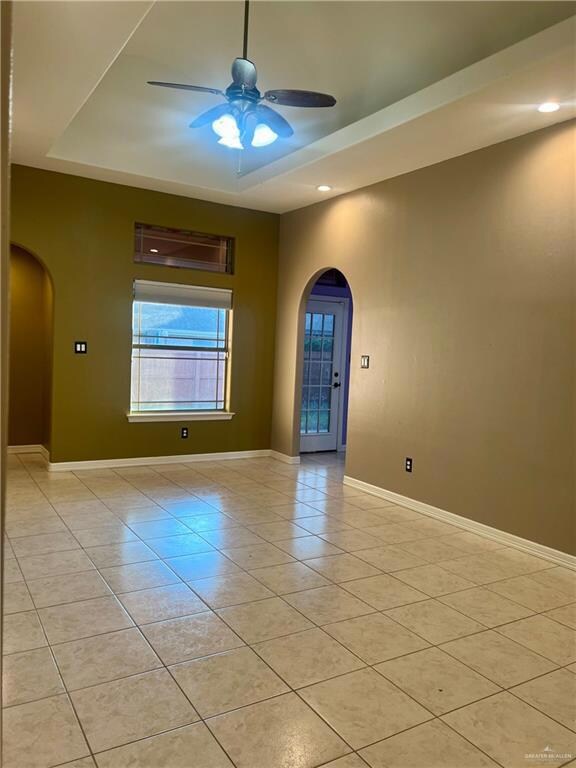 Unfurnished room featuring light tile patterned flooring, a raised ceiling, and ceiling fan