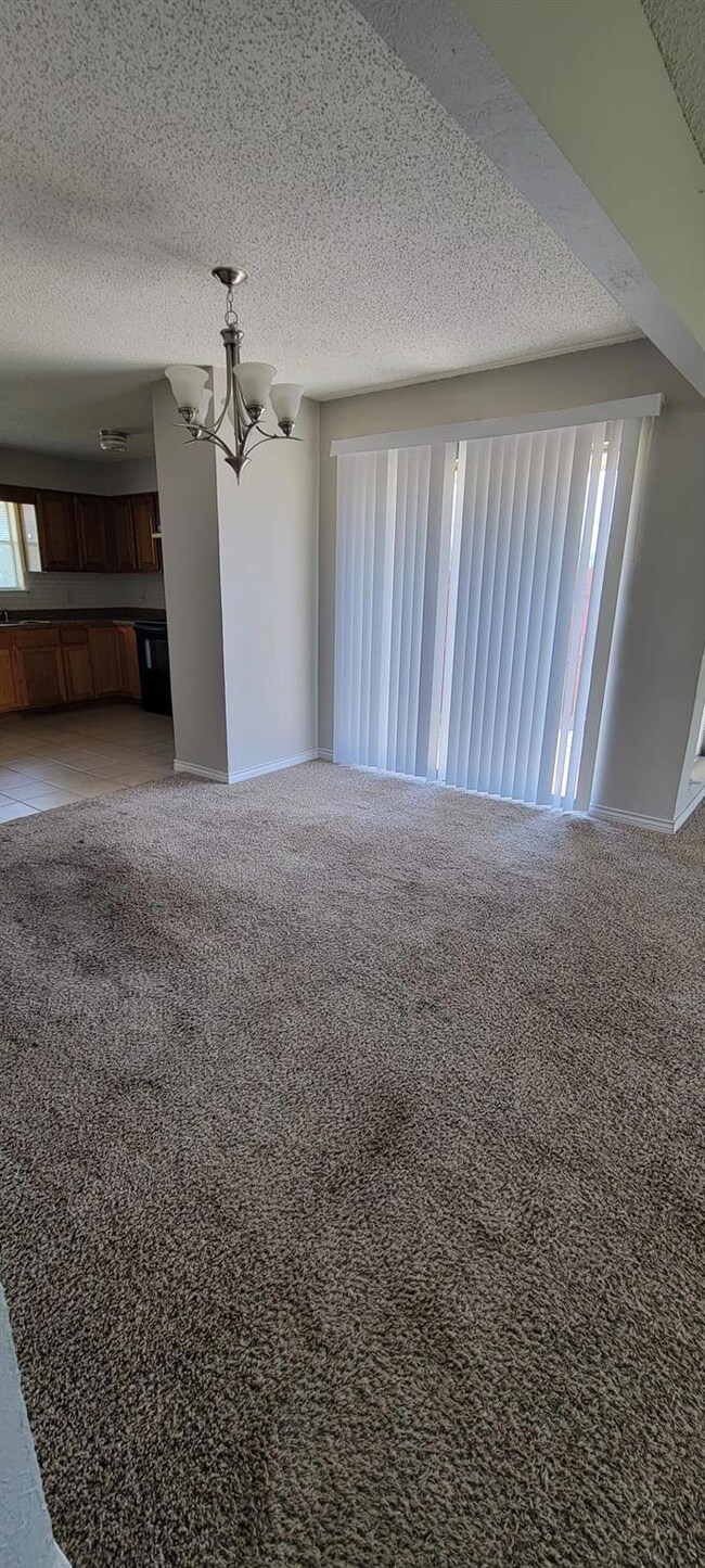 Unfurnished living room with a textured ceiling, an inviting chandelier, and carpet