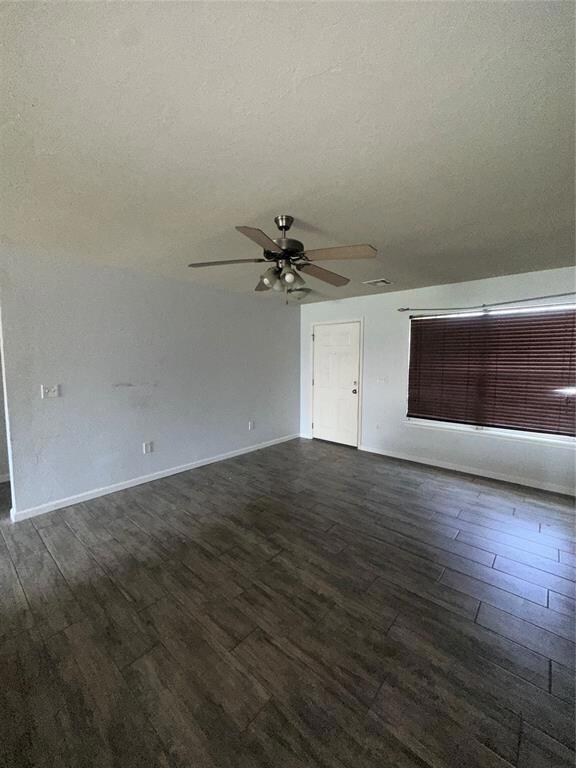 Unfurnished living room with a ceiling fan, dark wood-style floors, baseboards, and a textured ceiling