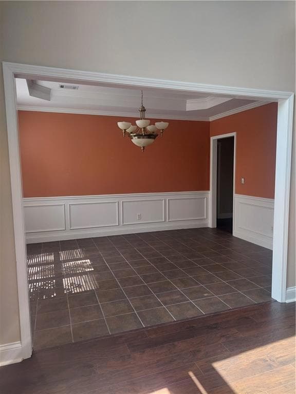 Empty room with crown molding, a chandelier, wainscoting, a tray ceiling, and dark wood-type flooring