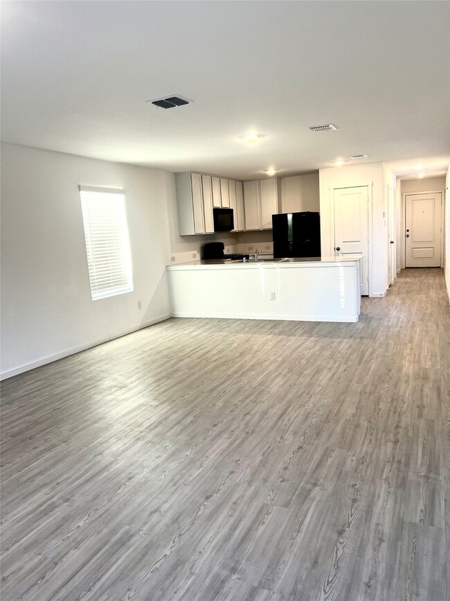 Kitchen featuring light wood finished floors, open floor plan, black appliances, a peninsula, and light countertops