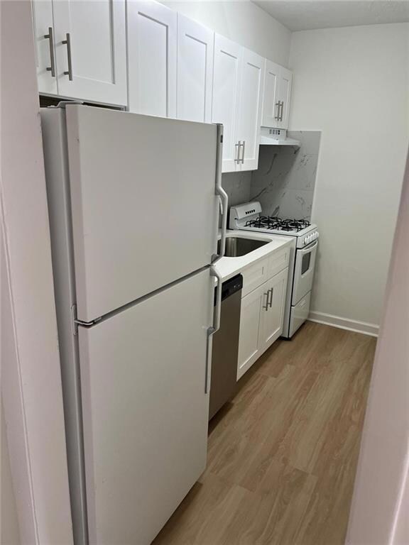 Kitchen with white appliances, light wood-style flooring, white cabinets, under cabinet range hood, and light countertops