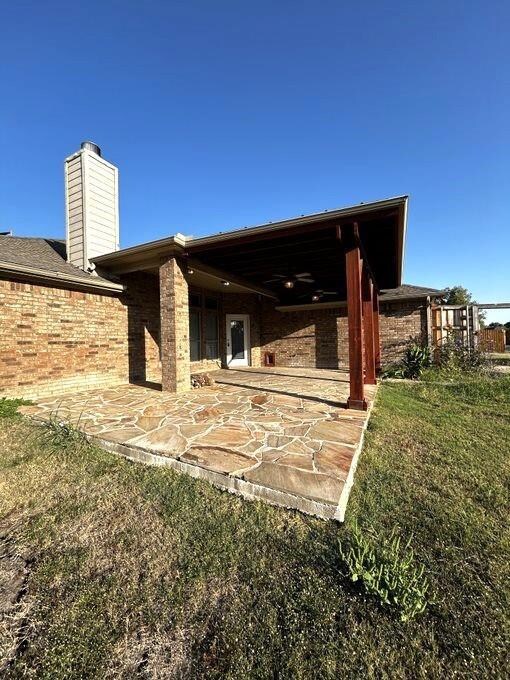 Back of house with ceiling fan, a lawn, and a pati