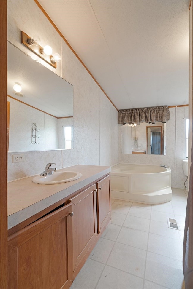Full bath featuring a garden tub, vanity, lofted ceiling, light tile patterned floors, and crown molding